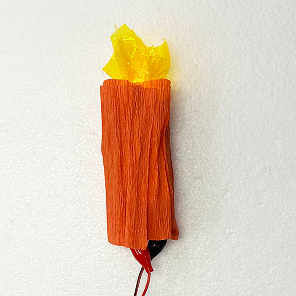 An orange candle made of creap paper with a cellophane top. There are black and red cables attached at the bottom.