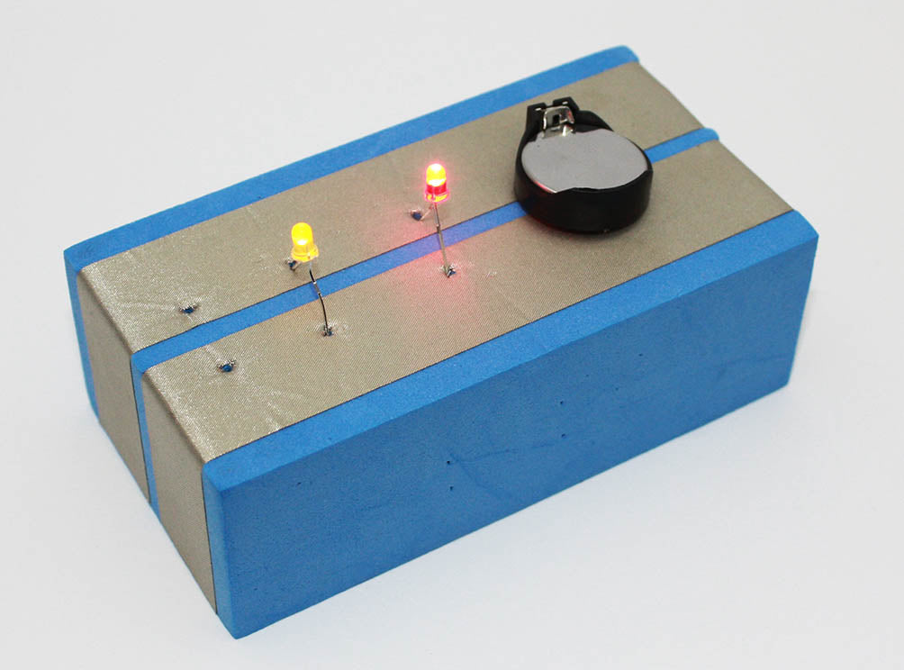 A foam block with two parallel pieces of conductive tape along the top. The battery is in the top as are 2 LEDs one yellow and one red