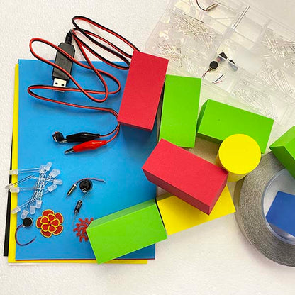 Picture of a jumble or components including 2 Red foam blocks, 3 green foam blocks, a USB cable with alligator clips, LEDs, motors, conductive tape 