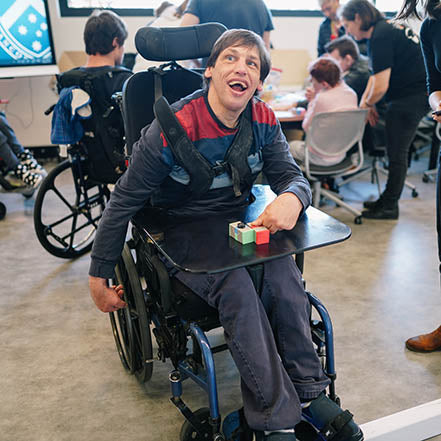 Man in a wheelchair smiling with a TapeBlock circuit on the tray that he has made