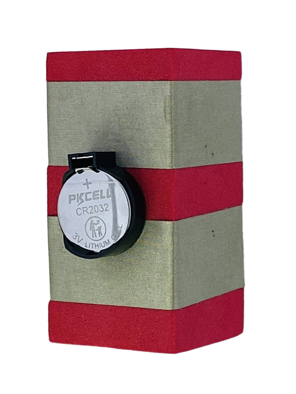 A red foam block with two parallel rows of conductive tape wrapped around it. It has a 3V battery in a black carrier in in the middle of the front of the block