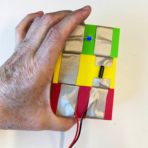 A close up of a hand holding 3 TapeBlocks together. Green with light, yellow with tilt and red attached to the USB cable TapeBlock