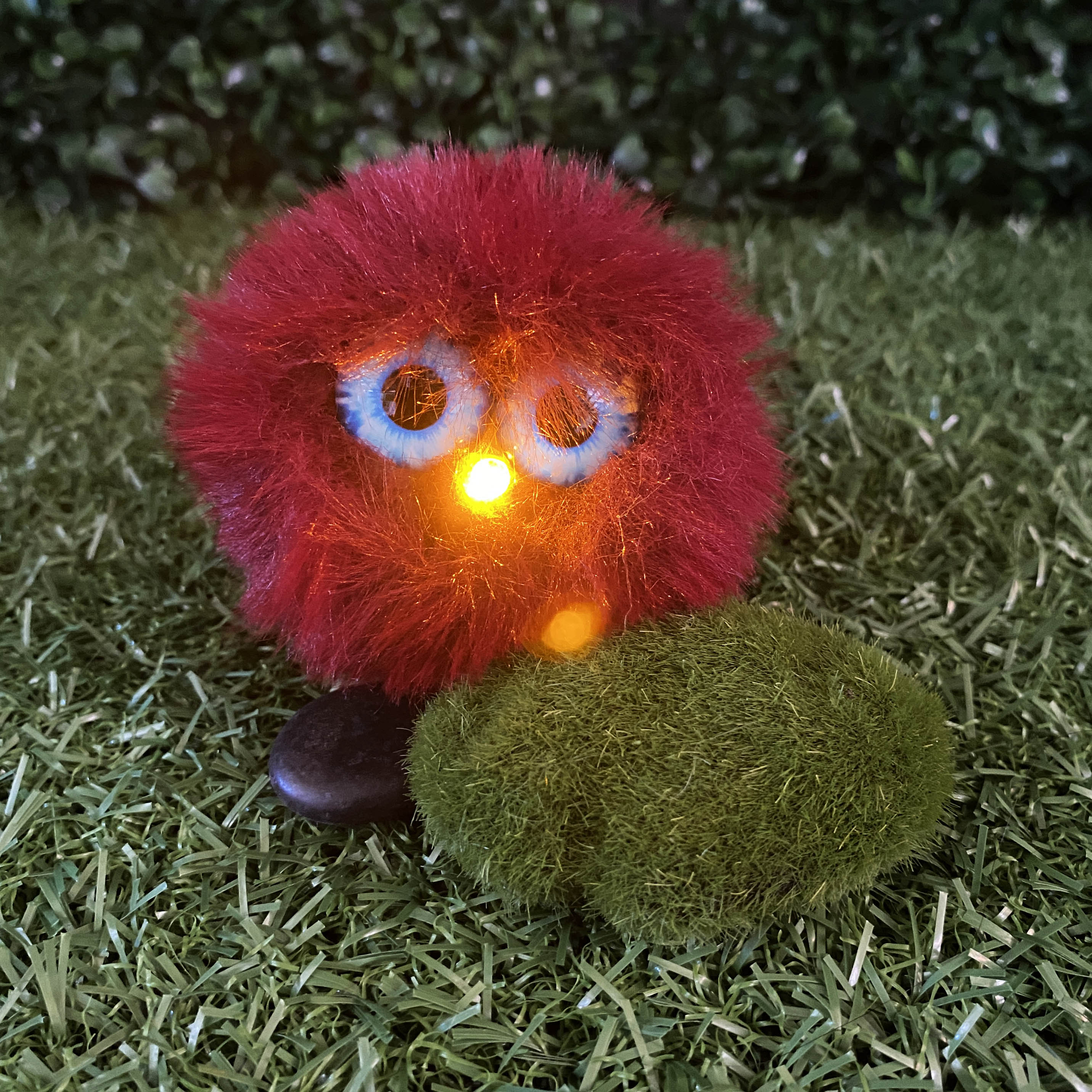 Round red fur TapeBlock with blue eyes and yellow light up nose, sitting on the grass