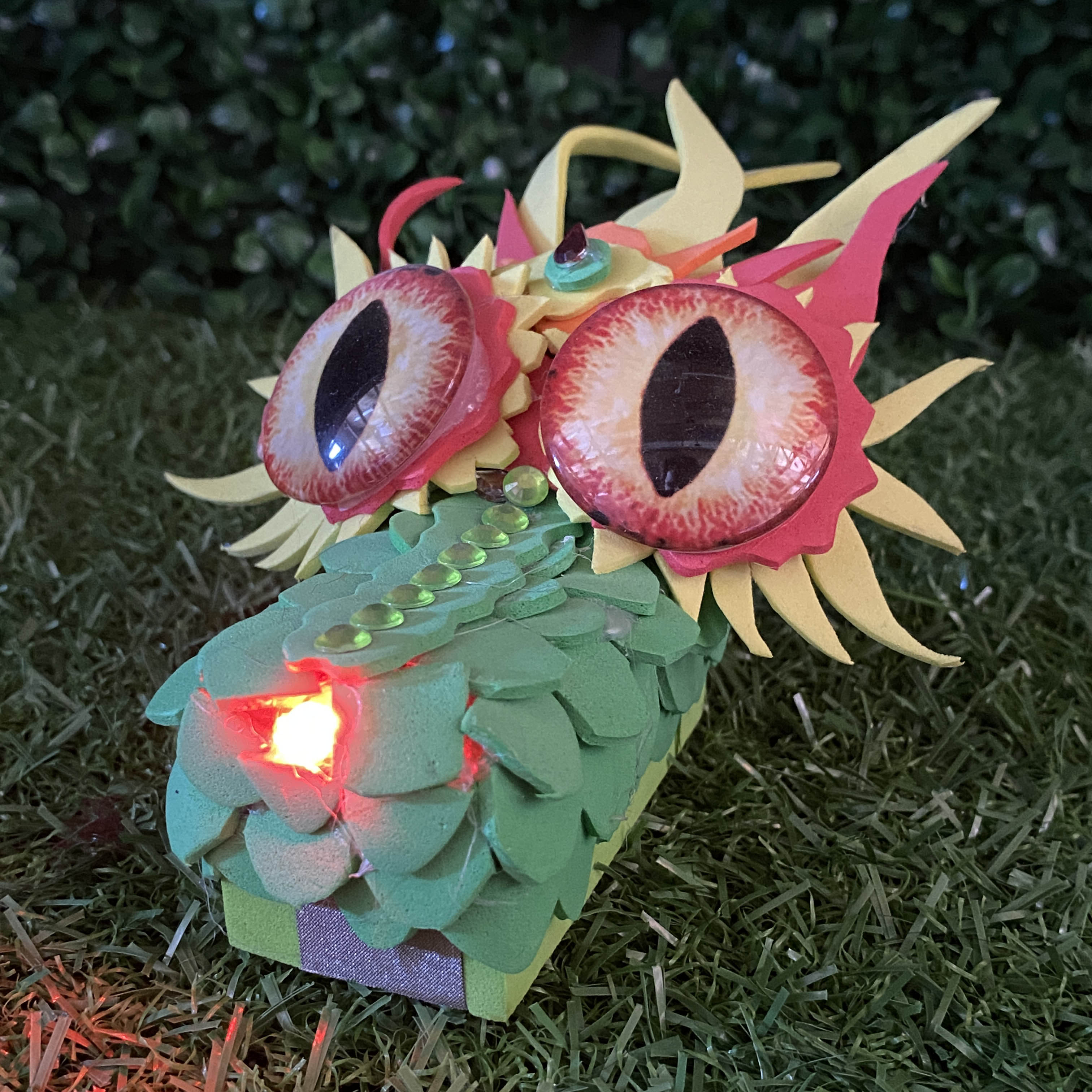 Green scale dragon head TapeBlock with red eyes and red light up nose. It is sitting in the grass