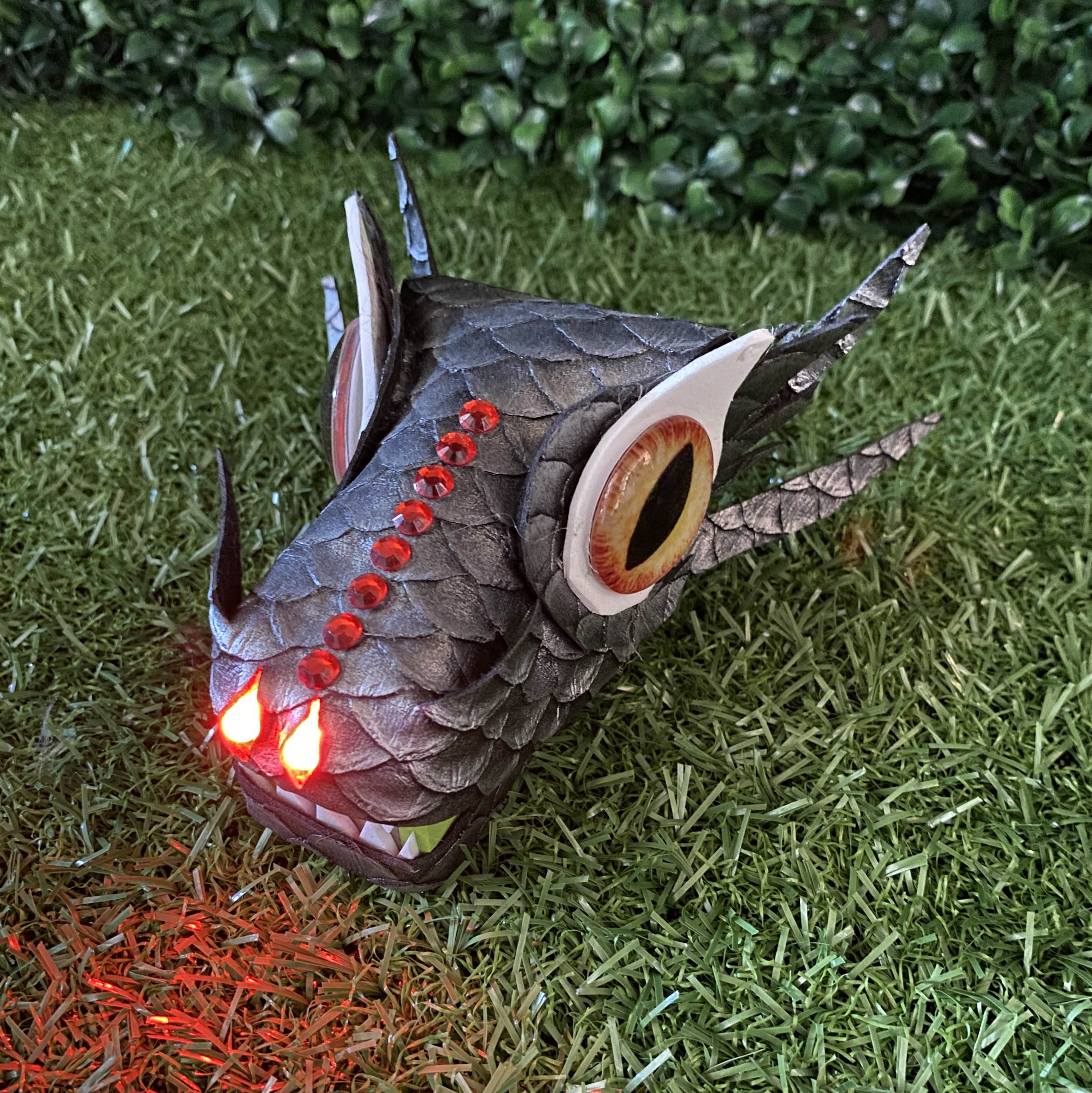 Grey scaly TapeBlock dragon with yellow glass eyes and red light up nostrils, It is sitting on the grass