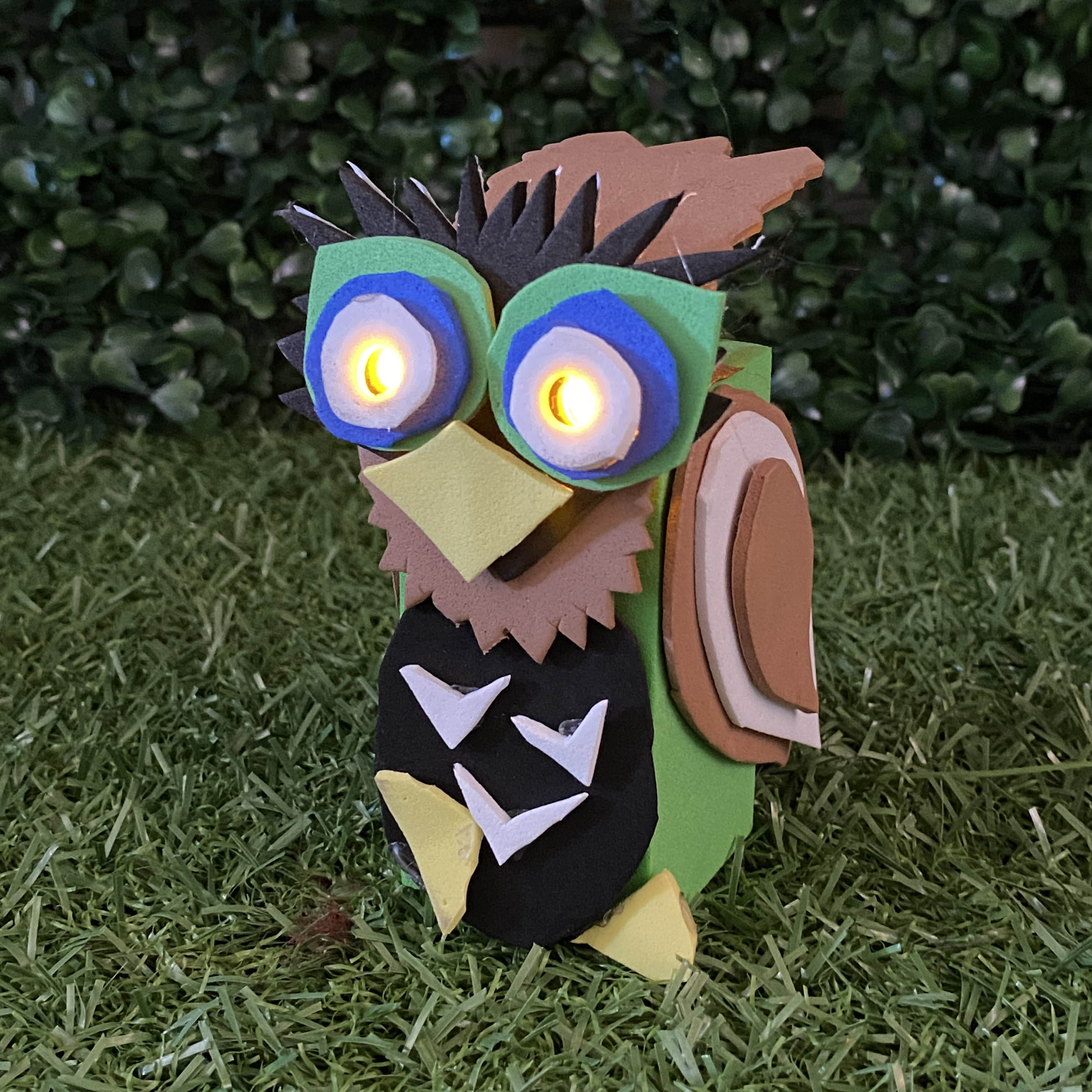 Owl TapeBlock with yellow beak and yellow light up eyes, It is sitting on the grass