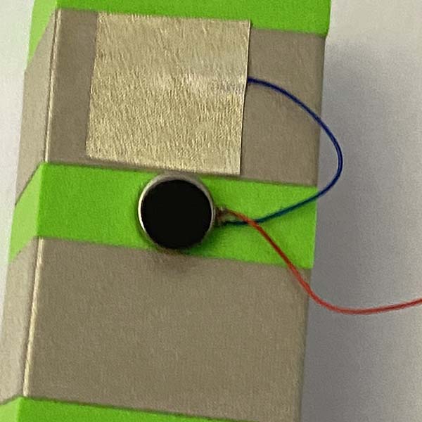 A close up of a button cell vibration motor with Two rows of sliver tape around a green foam block