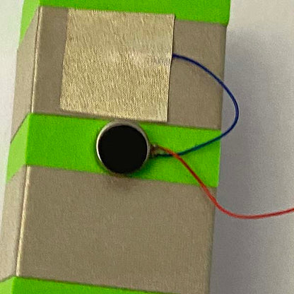 A close up of a button cell vibration motor with Two rows of sliver tape around a green foam block