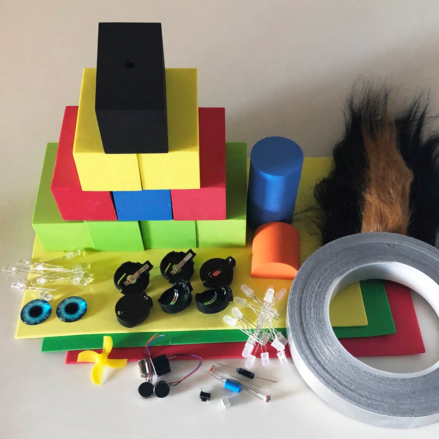 Contents of the TapeBlock making kit in a pile including Foam Blocks and sheet foam, LEDs, switches, motors and conductive tape, fur and eyes are included. This is more spaced out