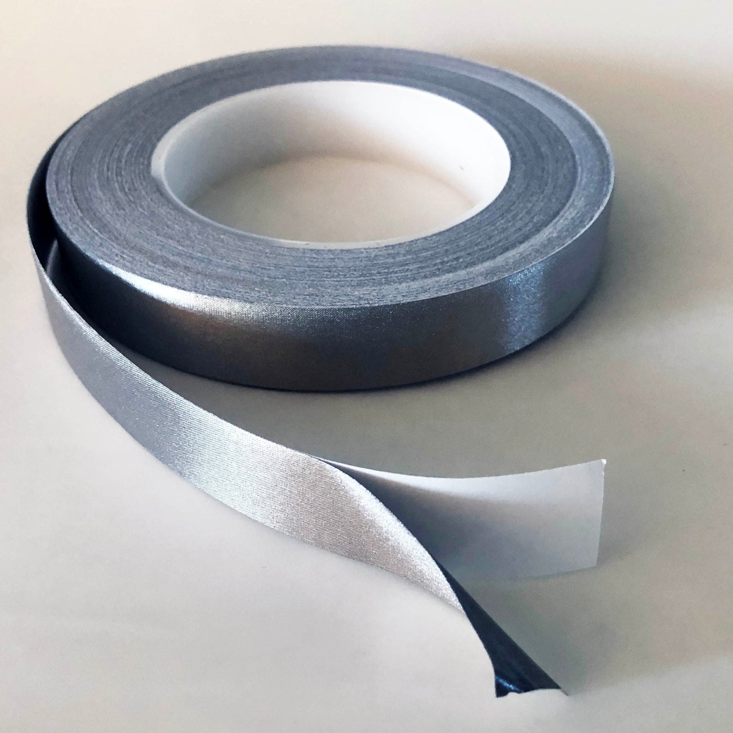 A Role of conductive tape which is open. There is an inch at the end showing the silver conductive tape separated from the white backing.