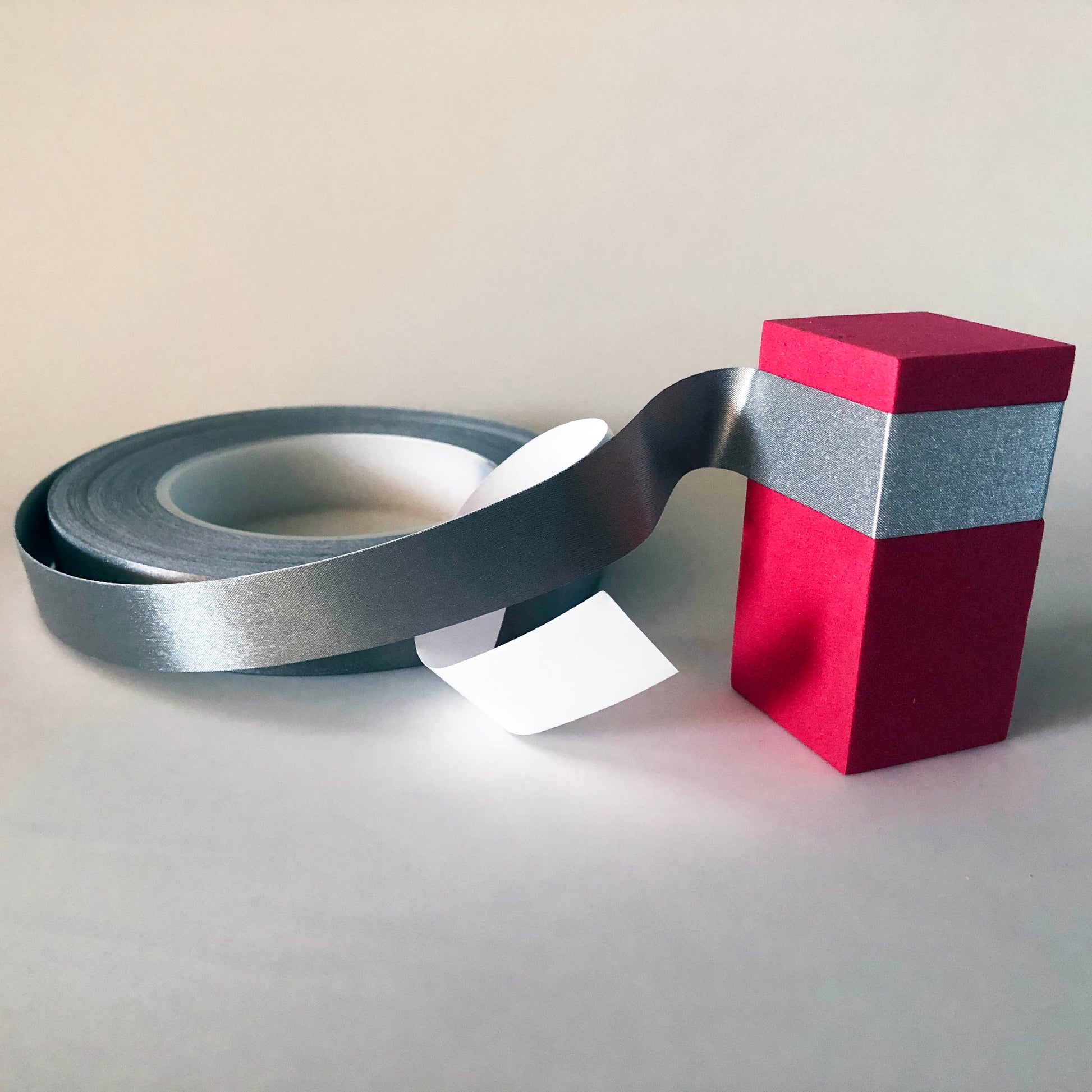 A roll of conductive tape with the end flexed around and attached to a red foam block. the white backing is still attached