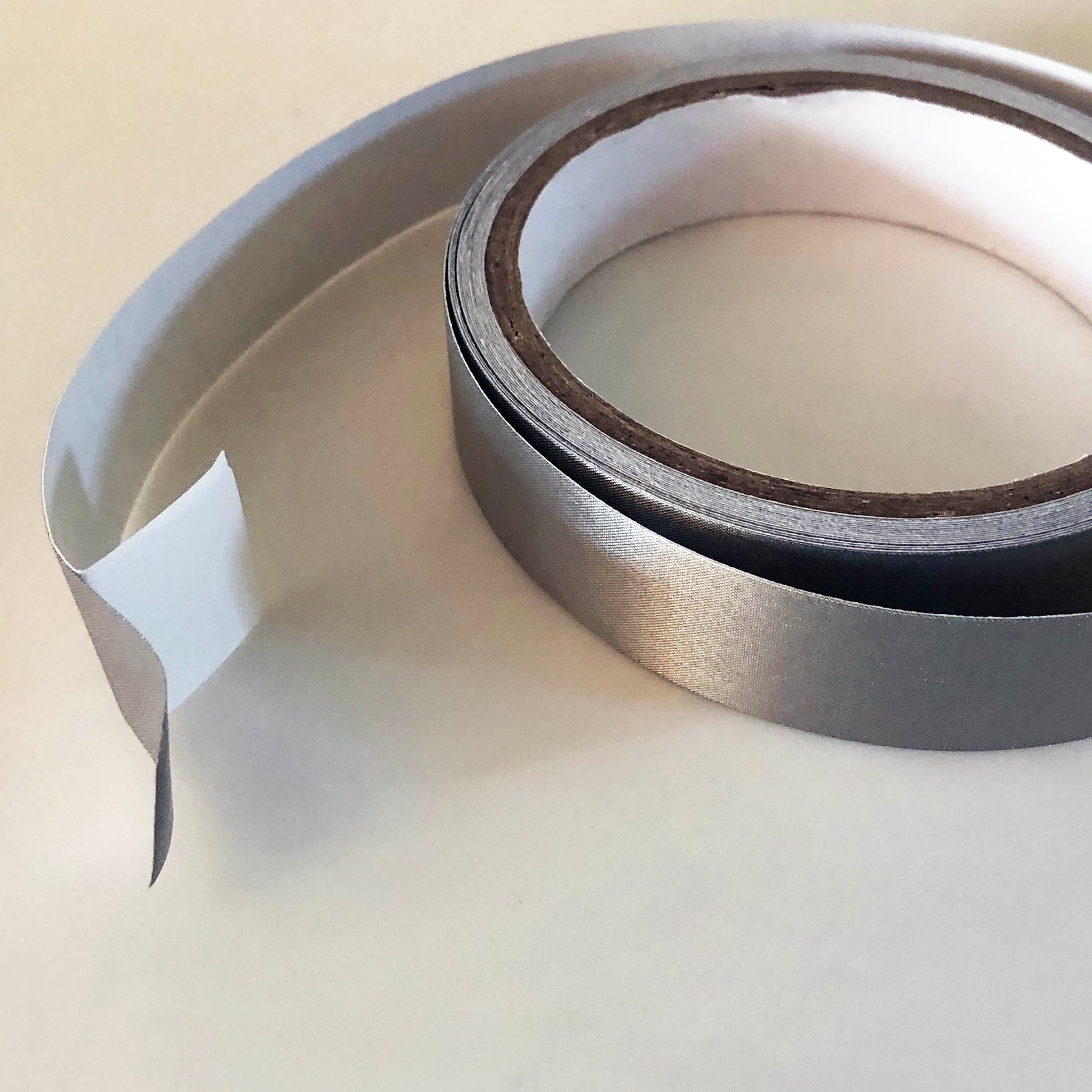 A 5 meter roll of conductive tape with an inch of the silver conductive tape separated from the white backing