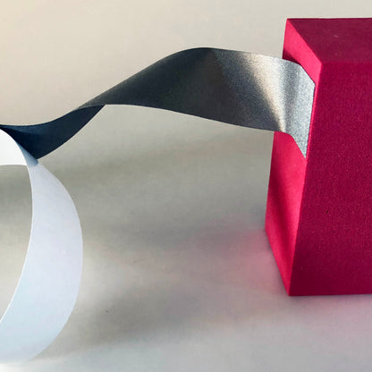 A flexible section of conductive tape is attached to a red block while it is still attached to the white backing